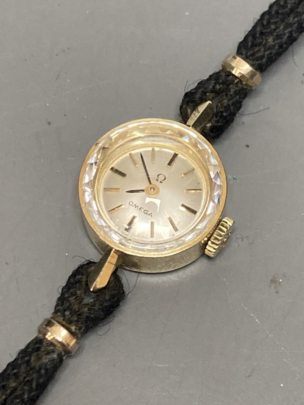 A ladys 14k Omega manual wind wrist watch, on twin strand fabric strap, case diameter 13mm ex. crown, gross 7 grams.